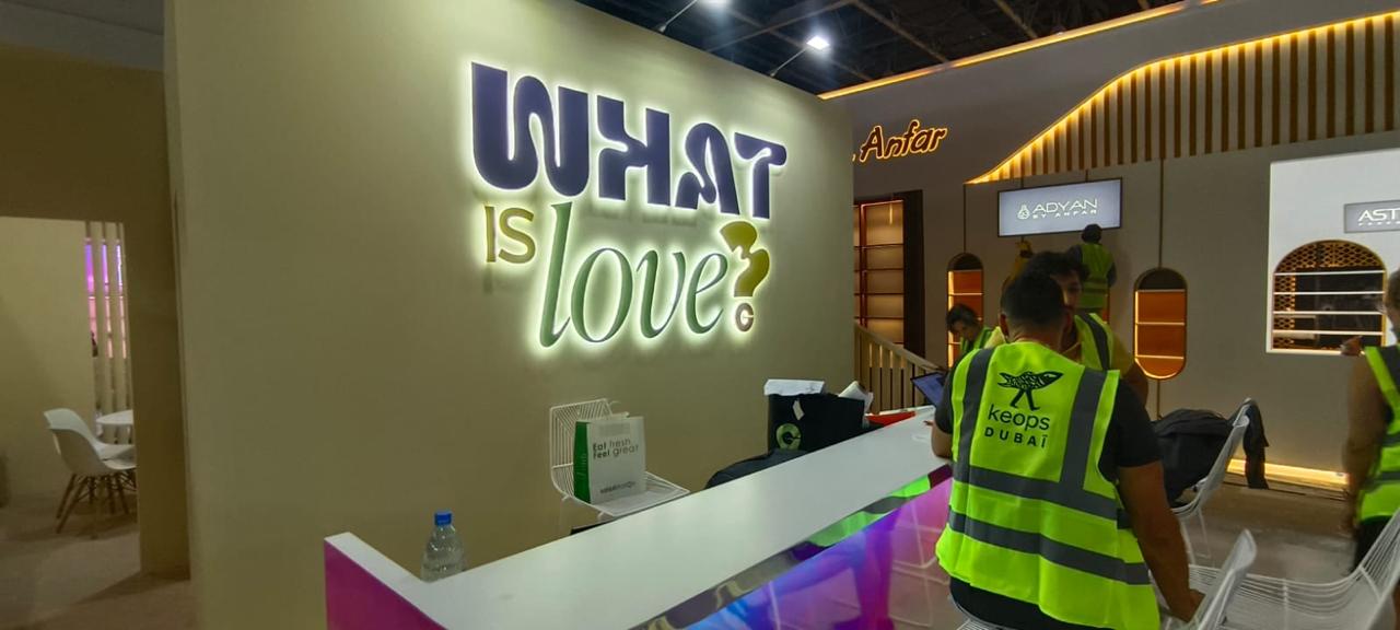 Backlit WHAT IS LOVE signage installed by Formset Advertising at a UAE exhibition booth with warm LED glow behind dimensional letters