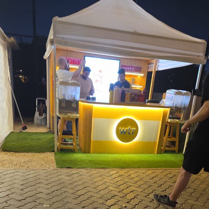 WTR backlit circular logo sign glowing on a yellow event booth at an outdoor night market in the UAE