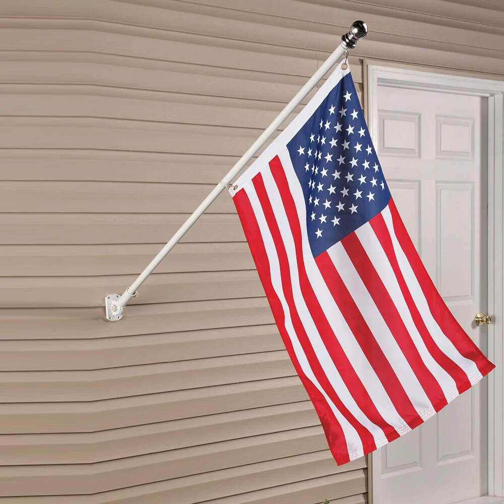 An American flag mounted on a white wall-mounted pole attached to beige siding next to a white door.
