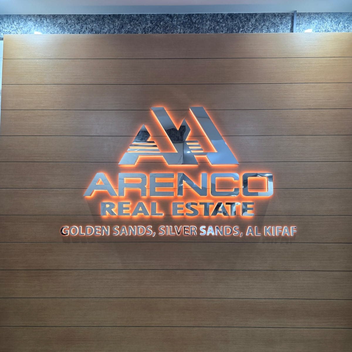 ARENCO Real Estate cutout letters and triangle logo with orange halo glow mounted on wood panel reception wall
