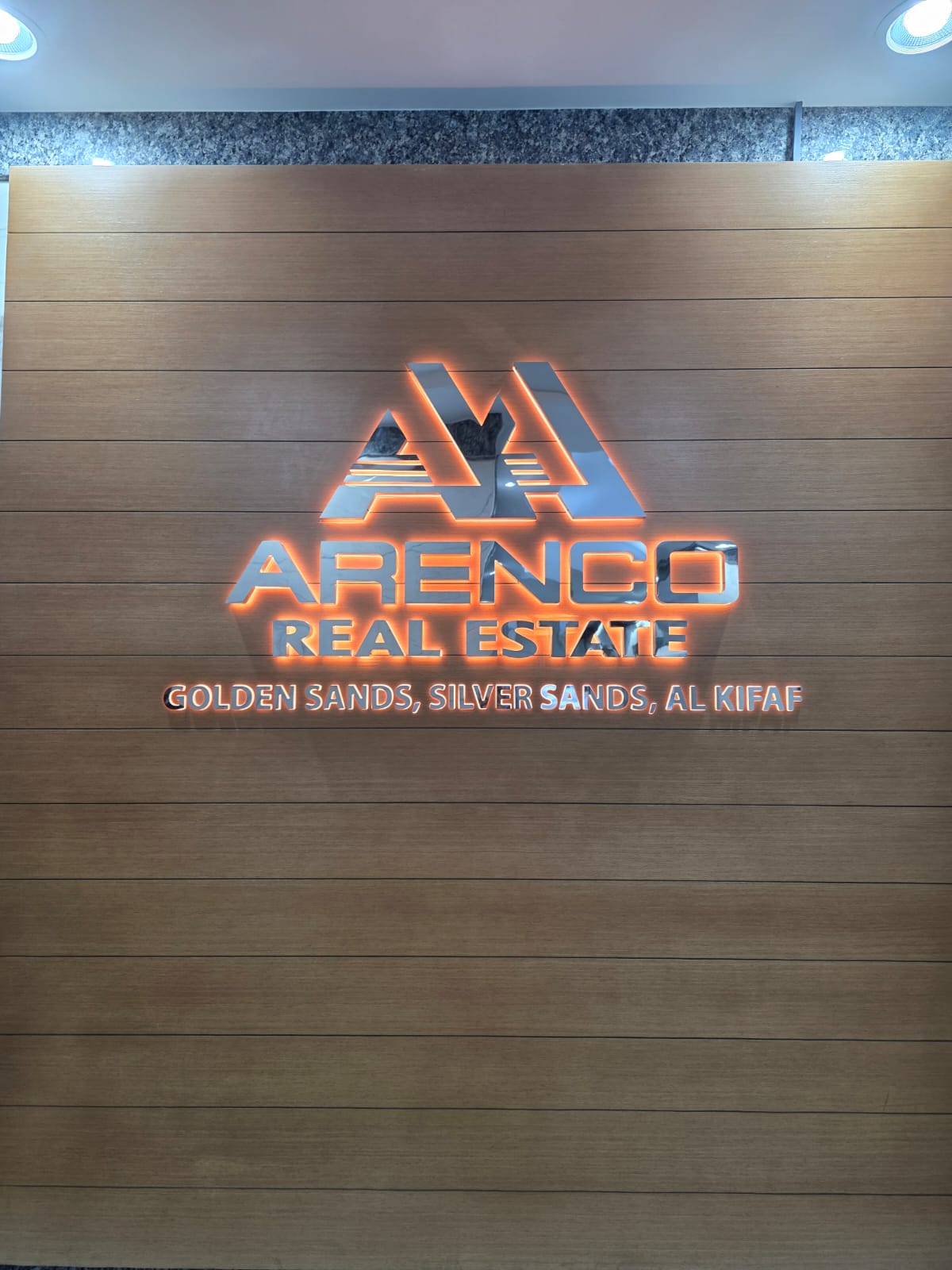 ARENCO Real Estate cutout letters and triangle logo with orange halo glow mounted on wood panel reception wall